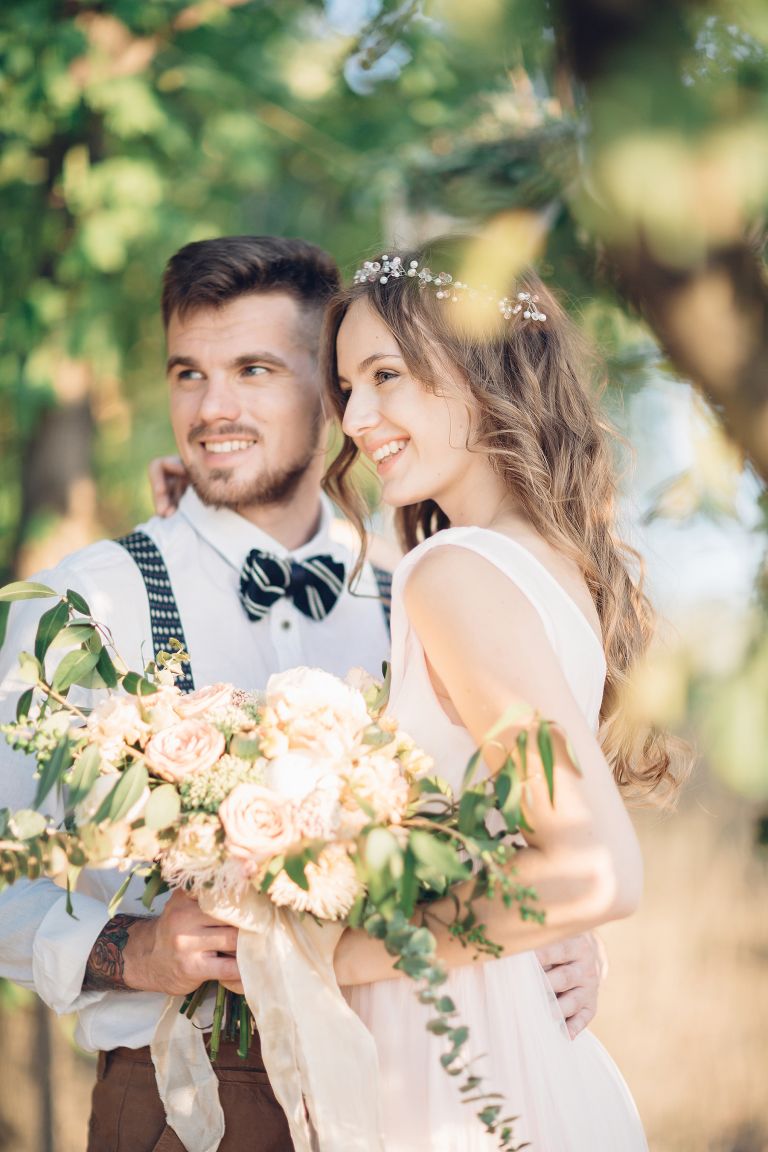 Bride and groom holding flowers beneath trees